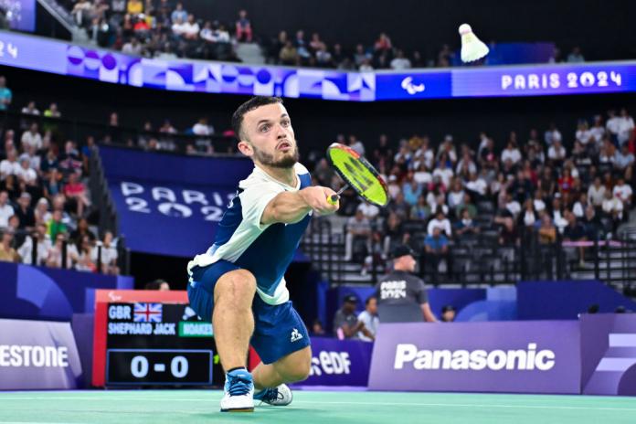 A man playing Para badminton lunges forward to hit the shuttlecock with his racket