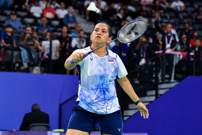 A woman holds a badminton racquet and aims towards a shuttlecock.