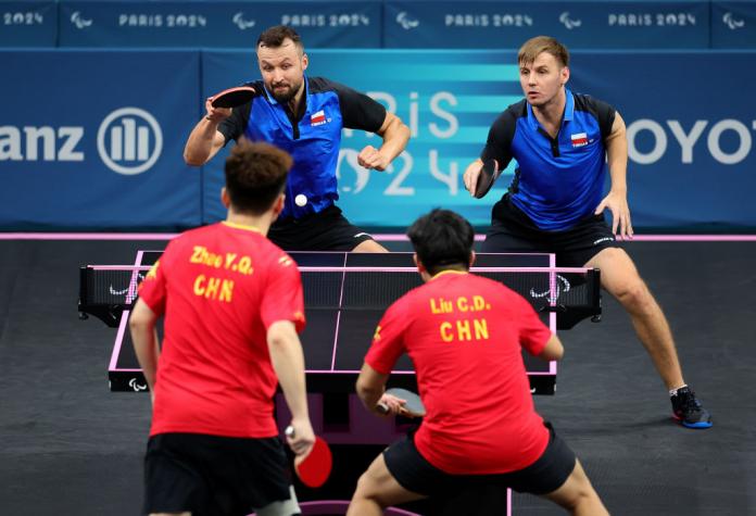 Four men play table tennis, two in red and two in blue