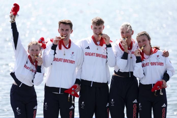 Cinco remeros con chaquetas blancas y mordiendo sus medallas de oro celebran su victoria