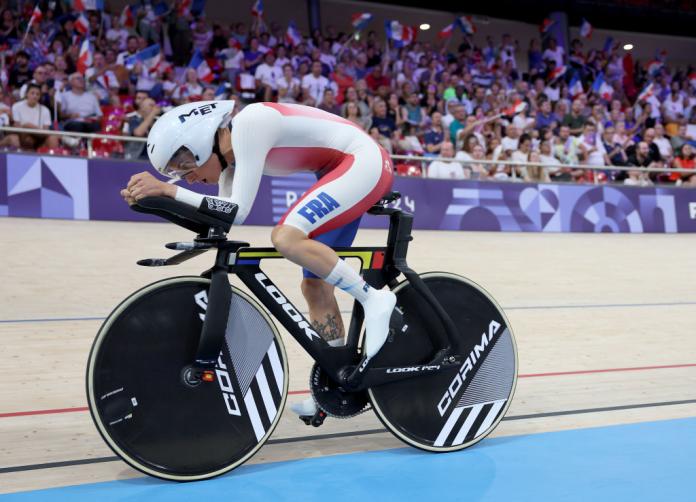 A woman rides a bike on an indoor track, with a big crowd in the stands