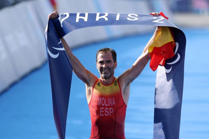 A man holds up a finish line banner that says "Paris 2024"