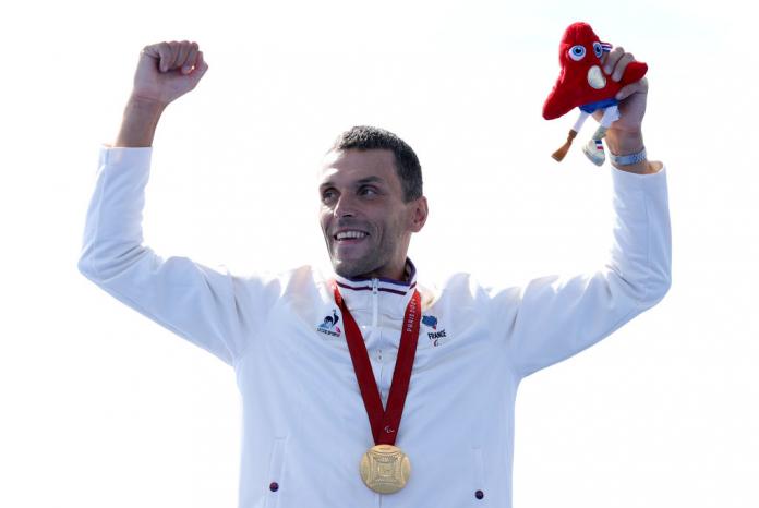 Para triathlete Alexis Hanquinquant raising his arms in celebration on the medal podium 