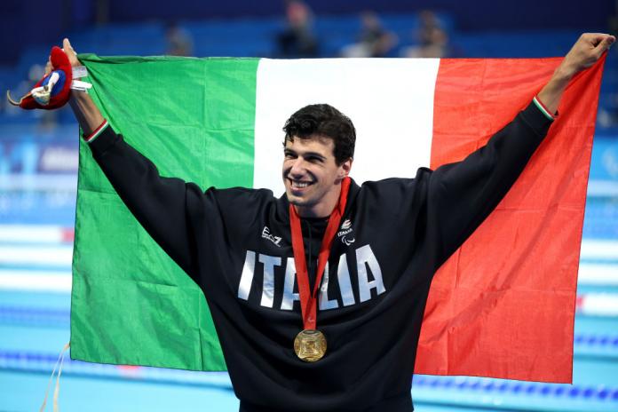 Para swimmer Simone Barlaam holding up the Italy flag with a gold medal around his neck