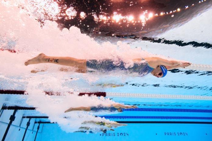 5 swimmers with their arms and legs outstretched, swimming in separate lanes in a pool