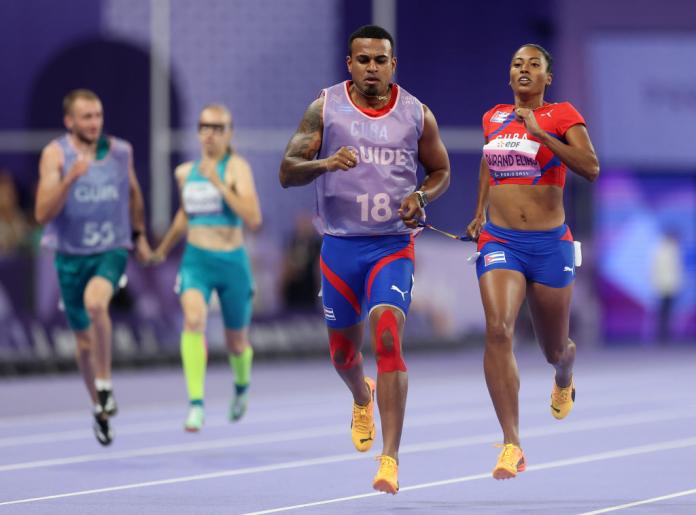 A man and a woman run down a purple track, each holding one end of a rope tether
