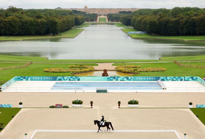 Una vista panorámica del lugar ecuestre Para París 2024, con una persona montando a caballo frente a jardines, un lago y un palacio