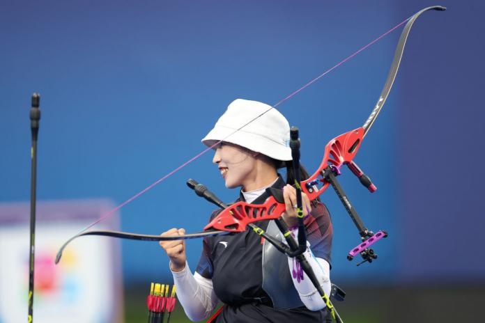 A woman smiles holds a Para archery bow in one hand while her other fist in clenched in satisfaction