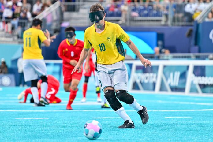 A man wearing a Team Brazil football uniform and an eye mask runs towards a football