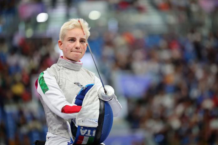 Bebe Vio sitting with her fencing mask in her hand and staring into the distance 