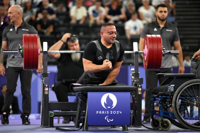 A man on a powerlifting bench sits up and clenches his fist in satisfaction