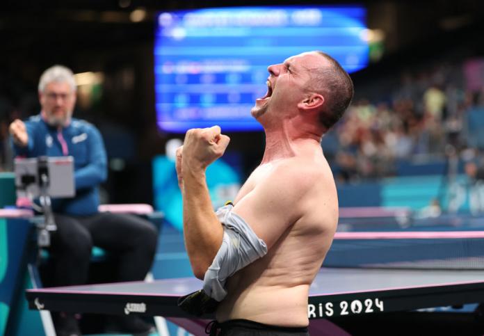 A male table tennis player takes off his shirt in celebration at winning a gold medal