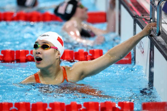 woman in goggles and speedo cap holds on to the edge of the pool and looks up shocked
