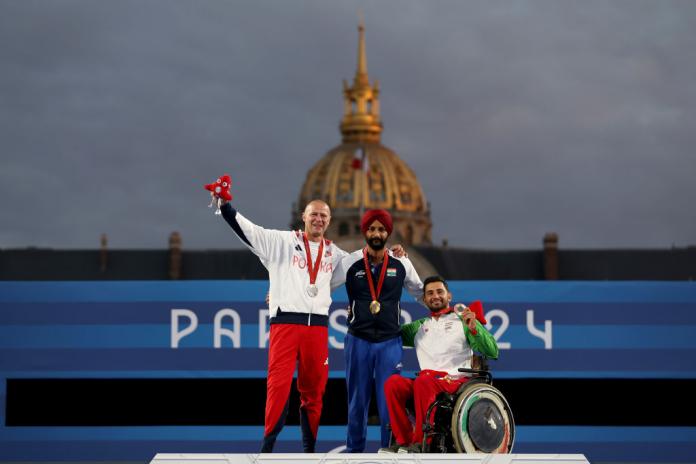 Three men stand on a podium, wearing medals