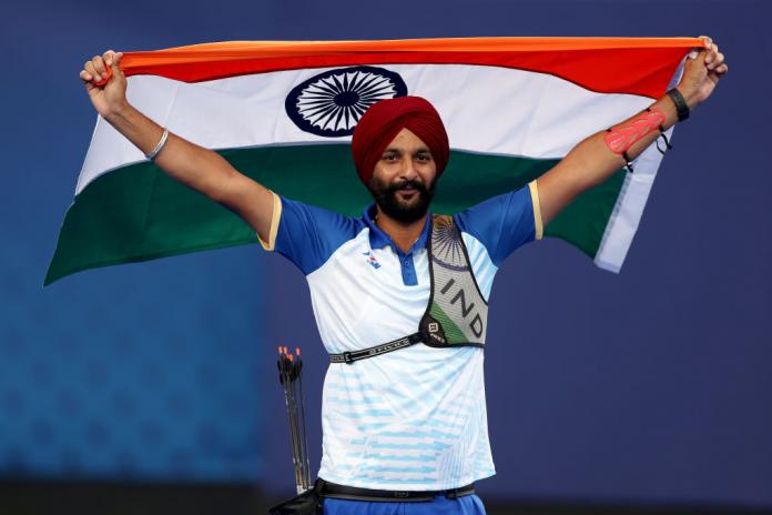 A man in a Team India uniform holds up an Indian flag behind his shoulders