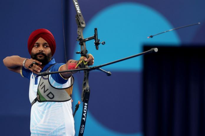 A man aims an archery bow, with the arrow he has shot in the air in front of him