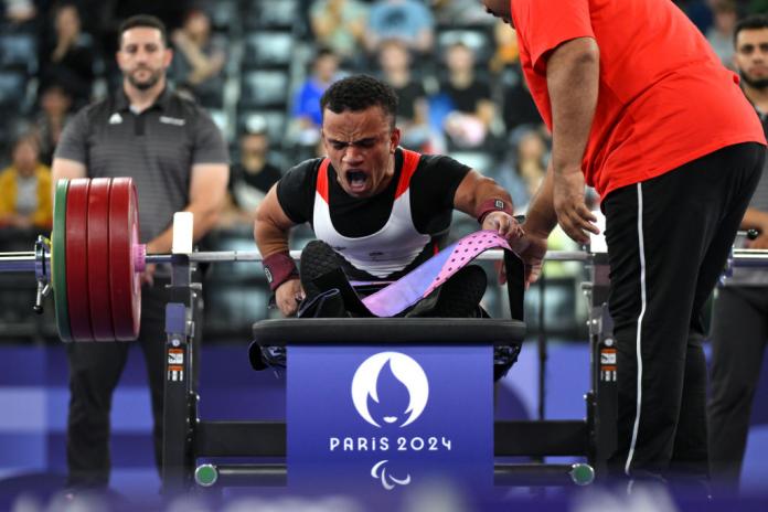 A man on a Para powerlifting bench sits up and yells in reaction to his performance