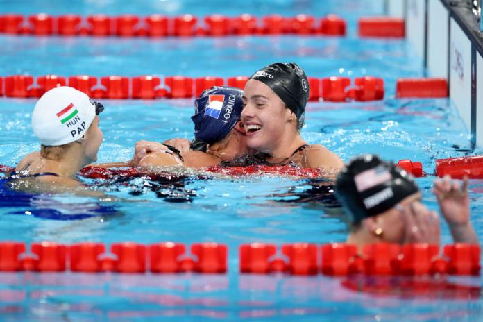 Three woman are in a pool after a Para swimming race. One smiles, and is hugged by another. 