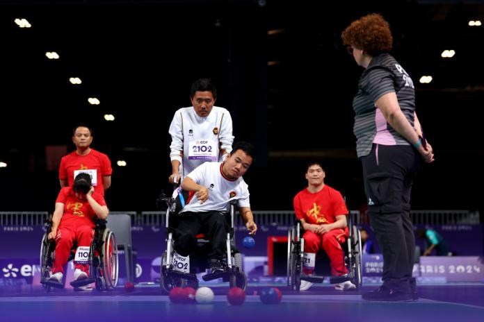 a male boccia player considers his shot while two opponents look on 