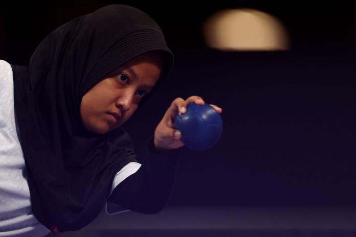 a female boccia player in a hijab aims a ball with her hand