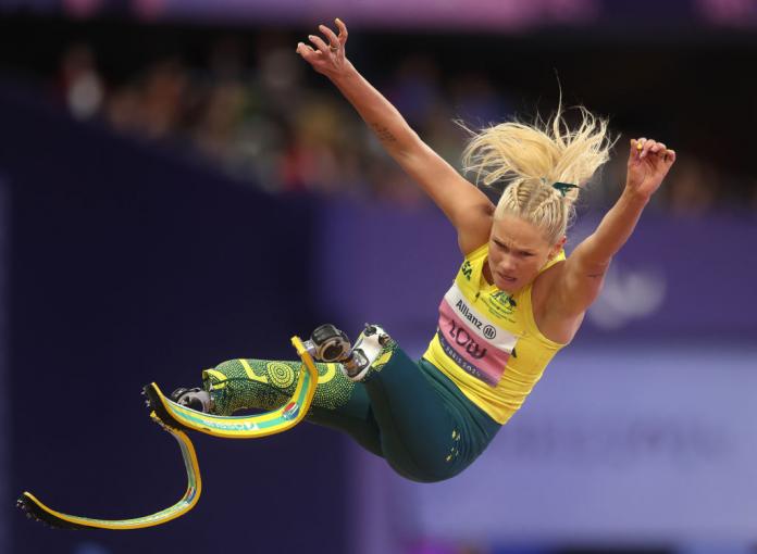 Una mujer con piernas protésicas está en el aire durante una competencia de salto de longitud
