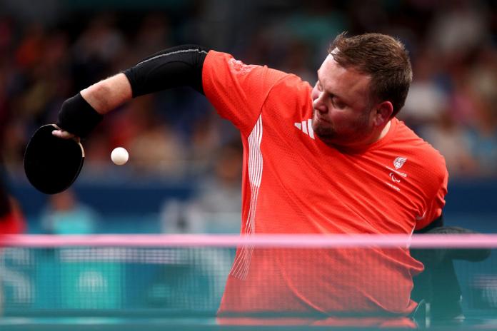 man in red reaches for a white table tennis ball with his paddle