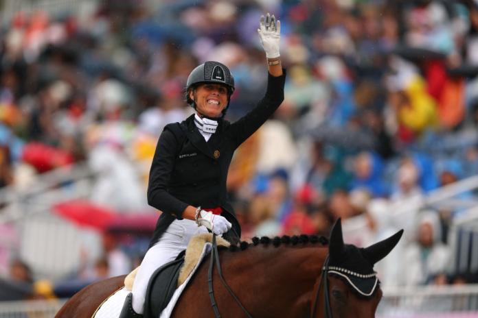 A female equestrian rider in a black jacket and helmet celebrates winning while sat on top of her horse