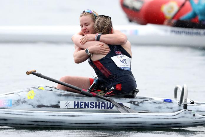 Two female British kayakers in dark blue vests  embrace while still in their kayaks on the water at the end of the race