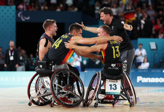 Tres jugadores de baloncesto en silla de ruedas y su entrenador, con uniformes del equipo de Alemania, extendieron los brazos para abrazarse en celebración