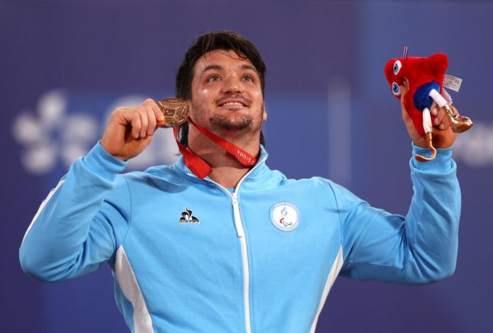 Gustavo Fernandez smiles and holds up his bronze medal