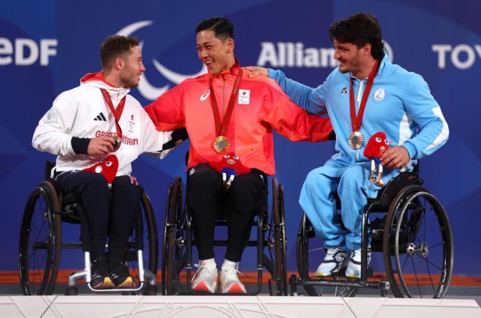Three wheelchair tennis players smiling and chatting on the podium