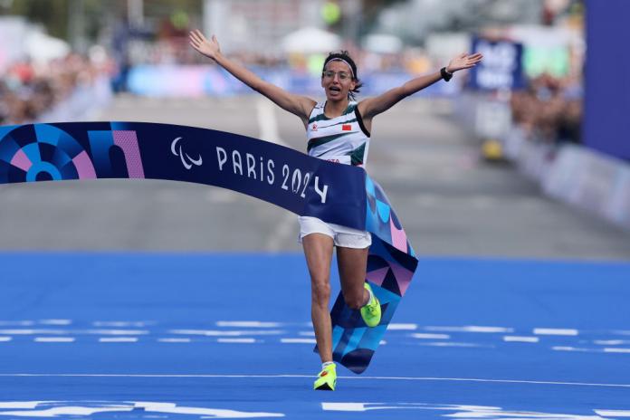 A woman runs across a finish line, her arms in the air