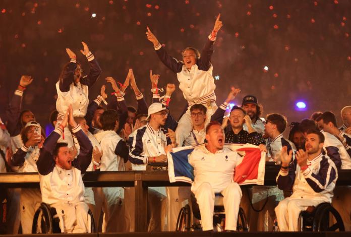 A group of Team France athletes surround a DJ, dancing and cheering