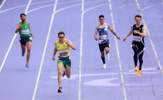Cuatro atletas masculinos compitiendo en una pista morada