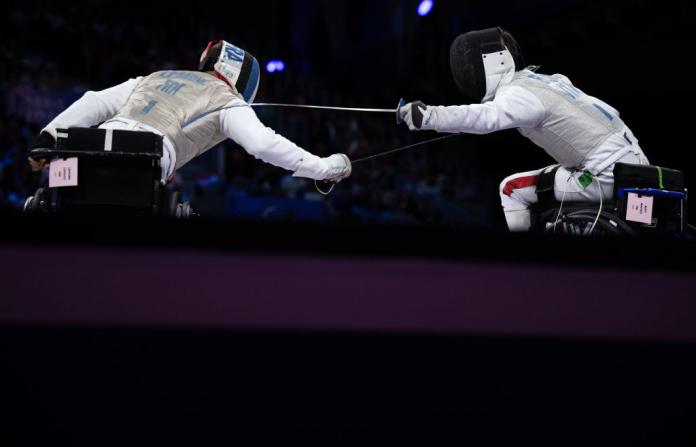 Two male wheelchair fencing athletes are in competition