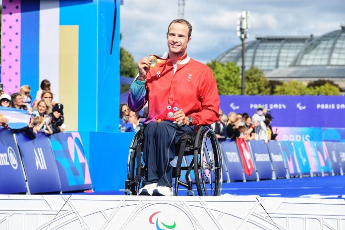 Wheelchair racer Marcel Hug holds up a gold medal on the podium and smiles