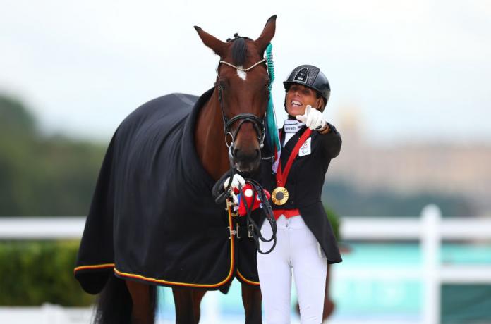 Michele George señala a la cámara después de recibir su medalla de oro. Su caballo está a su lado