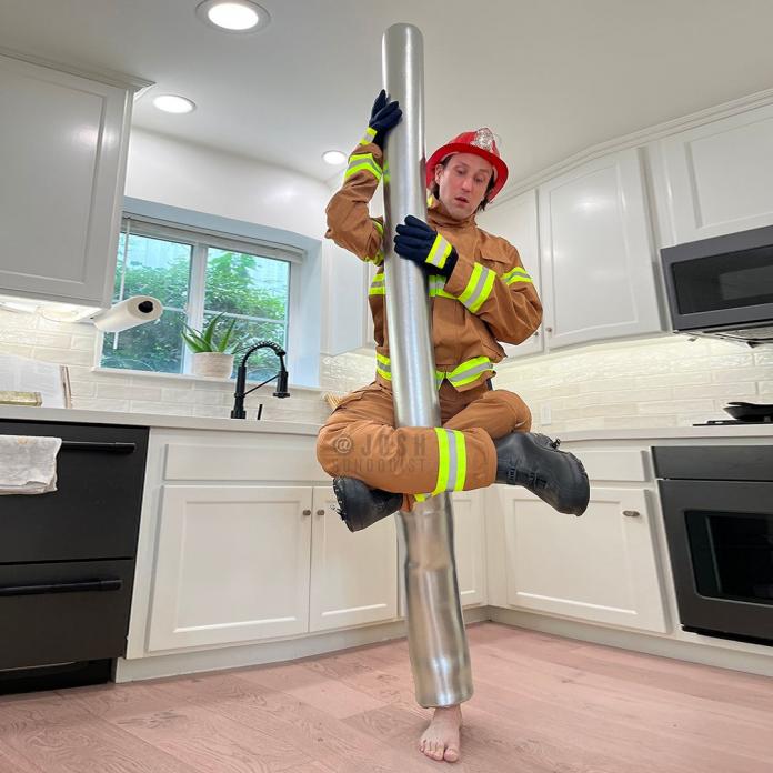 Josh Sundquist us wearing a costume of a firefighter sliding down a pole.