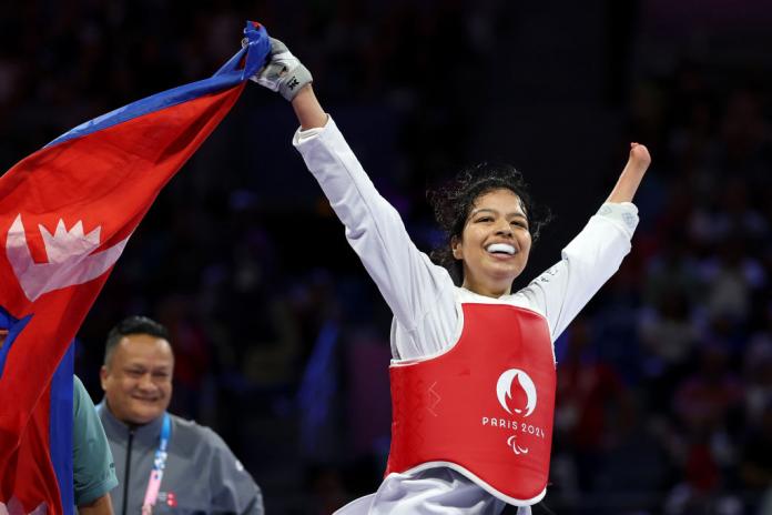 A female Para taekwondo athlete celebrates by holding Nepal's flag on the taekwondo mat