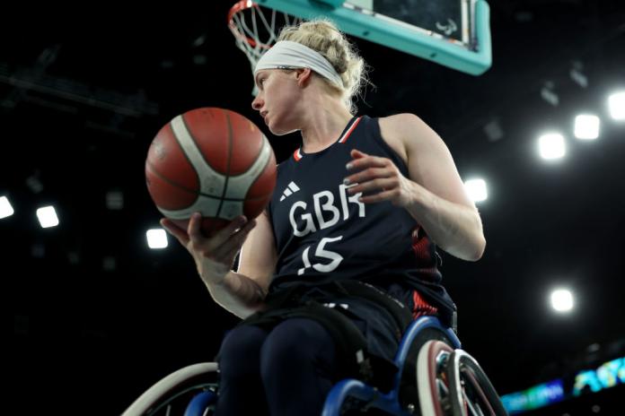 Robyn Love, una jugadora de baloncesto en silla de ruedas, mira a su derecha mientras sostiene una pelota