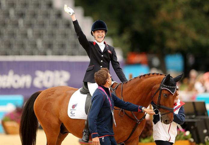A female Para equestrian athlete waves her hand while riding