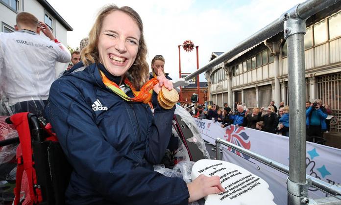 A female Para athlete poses for a photo by holding three gold medals next to her face during a parade