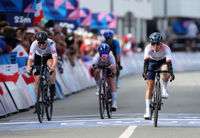 Three female Para cyclists competing at Paris 2024, with the athlete in the left crossing the finish line.