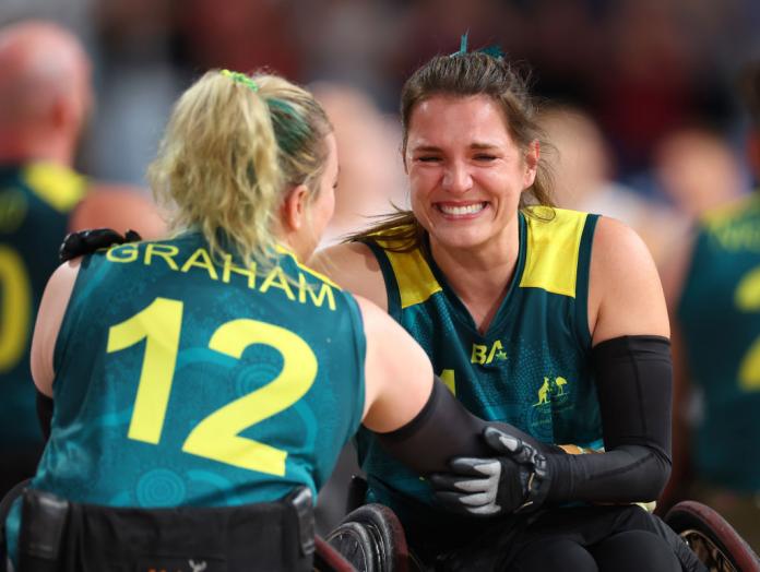 Two female wheelchair rugby players celebrate together on the court