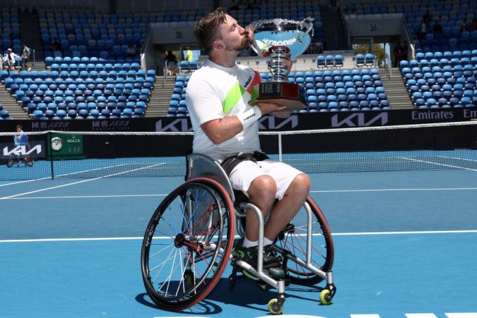 A male wheelchair tennis athlete kisses a silver trophy