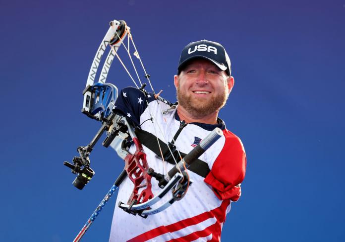 A male Para archer without arms smiles