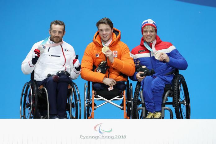 Three male athletes in wheelchairs pose for a photo on a podium.
