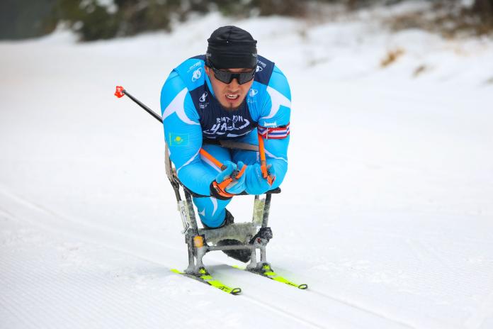 A male sit-skiing athlete wearing a blue skiing suit is competing at the Para Biathlon World Championships