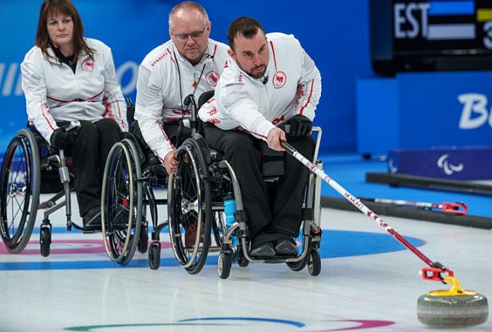 A male athlete is delivering a curling stone with a stick