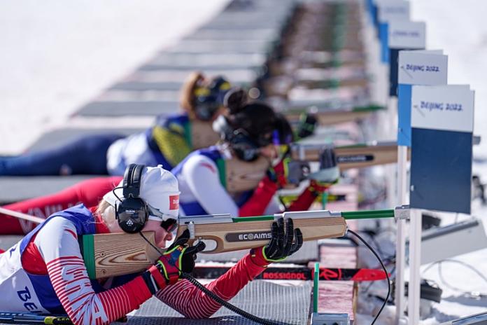 Three female athletes are in action at the shooting range during a biathlon competition